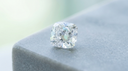 Cushion-cut lab-grown diamond on a pale grey surface, illustrating a cushion cut engagement ring stone