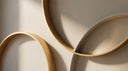 Interlocking warm gold and greige arcs in soft light, an abstract editorial backdrop for carabiner and connector necklaces