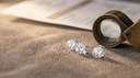 Loose round brilliant lab-grown diamonds with a brass jeweller's loupe on a warm greige atelier workbench