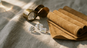 Loose colourless lab-grown diamonds in round, oval and emerald cuts beside a jeweller's loupe and suede ring roll on warm greige linen