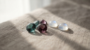Loose alexandrite gemstones showing teal-to-mauve colour change beside creamy moonstones on greige linen — June birthstones