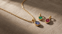 Solid gold cable-chain necklace on greige linen with gemstone birthstone charms ready to add — building a charm necklace