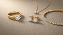 Flat-lay of lab-grown diamond jewellery in solid yellow gold — a solitaire ring, round diamond stud earrings, a diamond pendant necklace and a diamond tennis bracelet on warm greige linen
