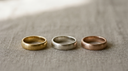 Three solid gold bands side by side — yellow gold, white gold and rose gold — showing the colour difference