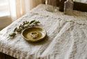 A lab-grown diamond solitaire engagement ring in solid gold on a ceramic ring dish over linen, in golden-hour light
