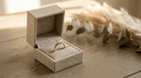 An open linen ring box presenting a solid-gold lab-grown diamond solitaire engagement ring, ready for a proposal