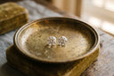 Two identical loose round brilliant diamonds side by side on an aged brass dish in warm window light