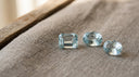 Loose pale sea-blue aquamarine gemstones, the March birthstone, on warm greige linen
