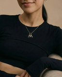 Person wearing a black top and gold necklace with a pendant against a beige background